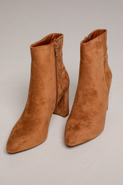 A pair of tan suede ankle boots with block heels and side zippers, displayed on a light gray studio background.