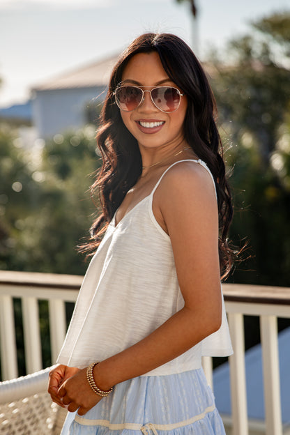 Woman wearing sunglasses and a white sleeveless top with a blurred outdoor background