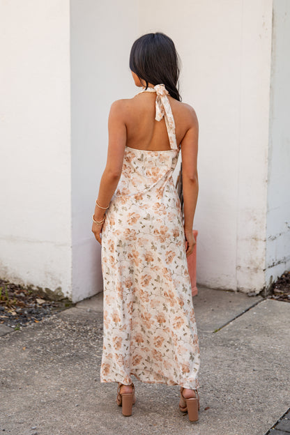 Woman wearing a floral dress standing against a white wall.