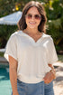 Woman wearing sunglasses and a white blouse with a denim skirt by a pool