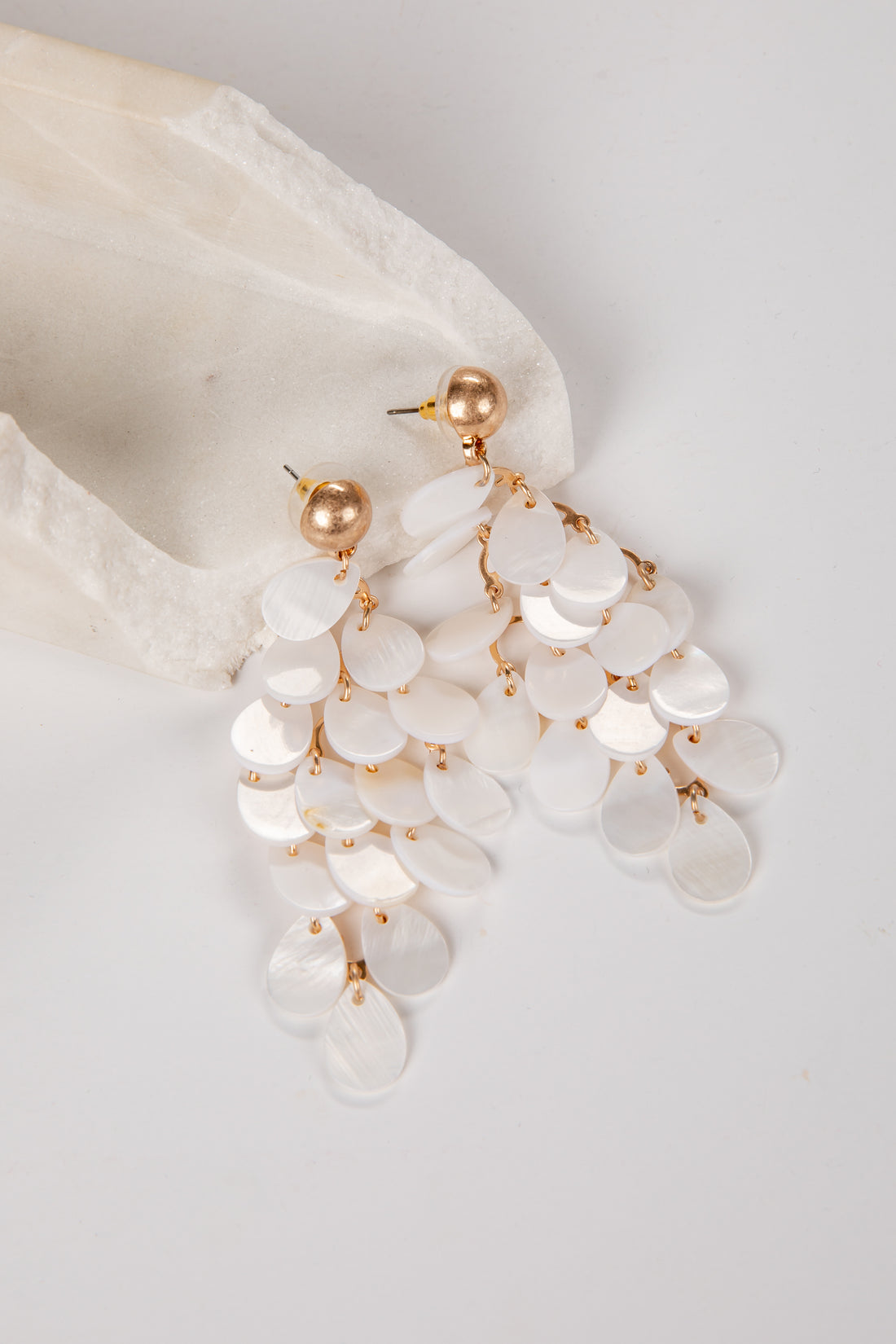 Pearl and gold earrings hanging from a white shell on a light gray background