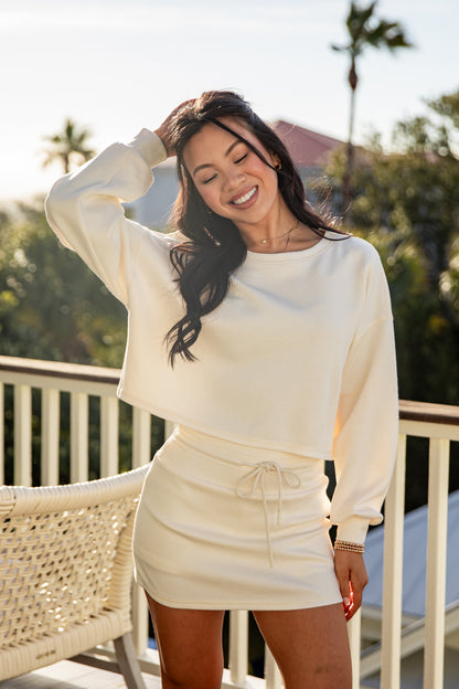 Woman in a cream-colored outfit standing outdoors with palm trees in the background