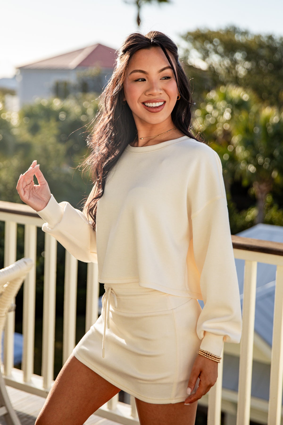 Woman in a white outfit standing on a balcony with greenery in the background