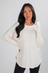 Woman wearing a cream-colored long-sleeve top against a plain background