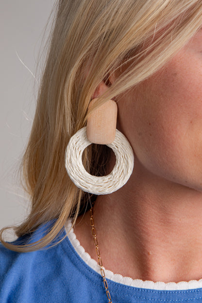 Close-up of a woman wearing a beige and white circular earring with a blue top.