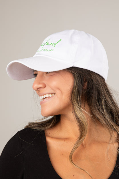 Woman wearing a white cap with green text on a neutral background