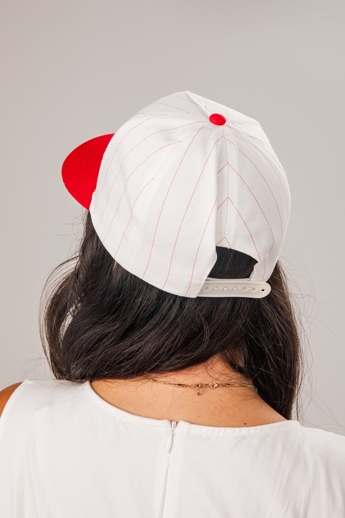 Person wearing a white cap with red accents on a plain background