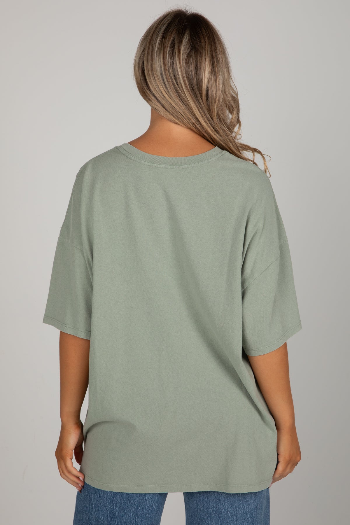 Person wearing a green t-shirt and blue jeans on a gray background
