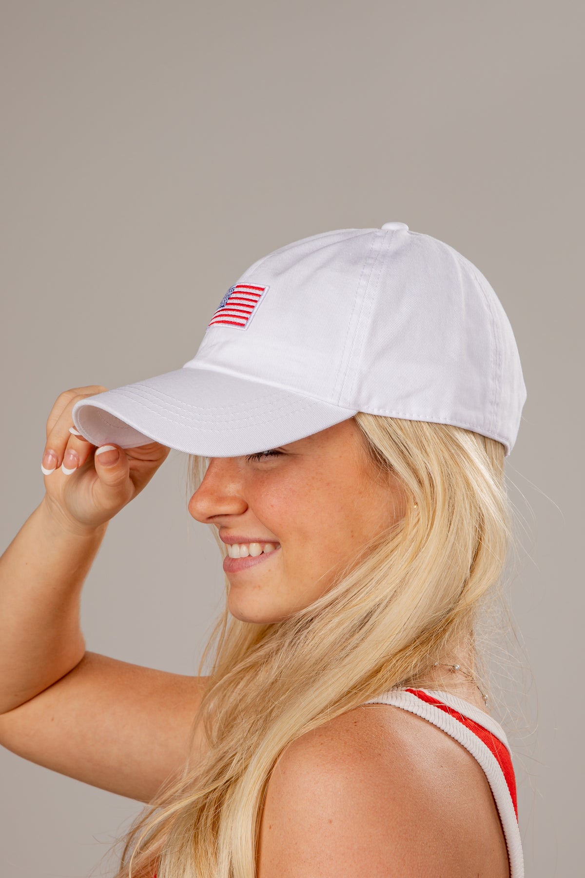 Woman wearing a white cap with a small flag design on a plain background