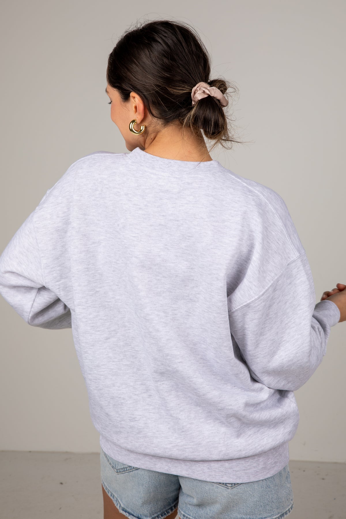 Person wearing a light gray sweatshirt and light blue jeans against a plain background
