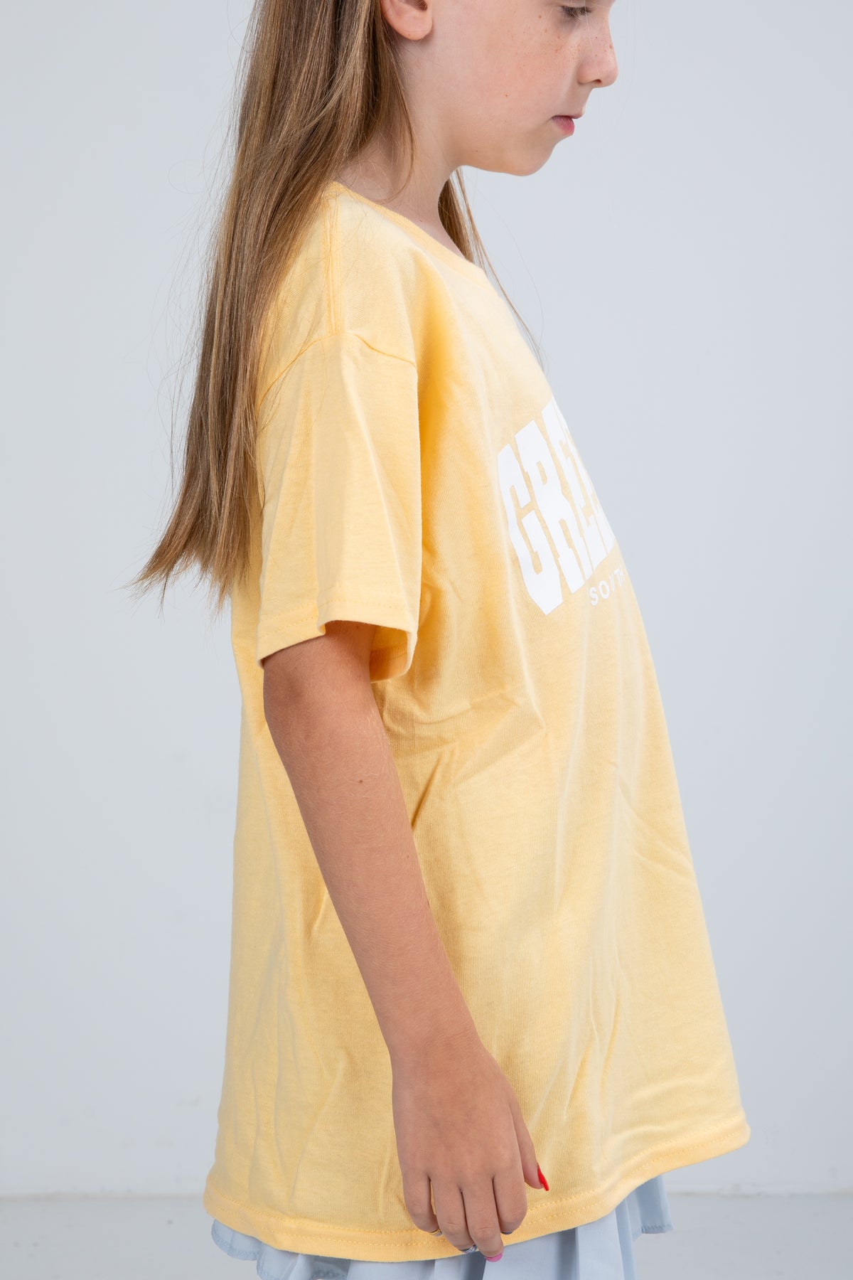 Child wearing a yellow t-shirt with text on a plain background
