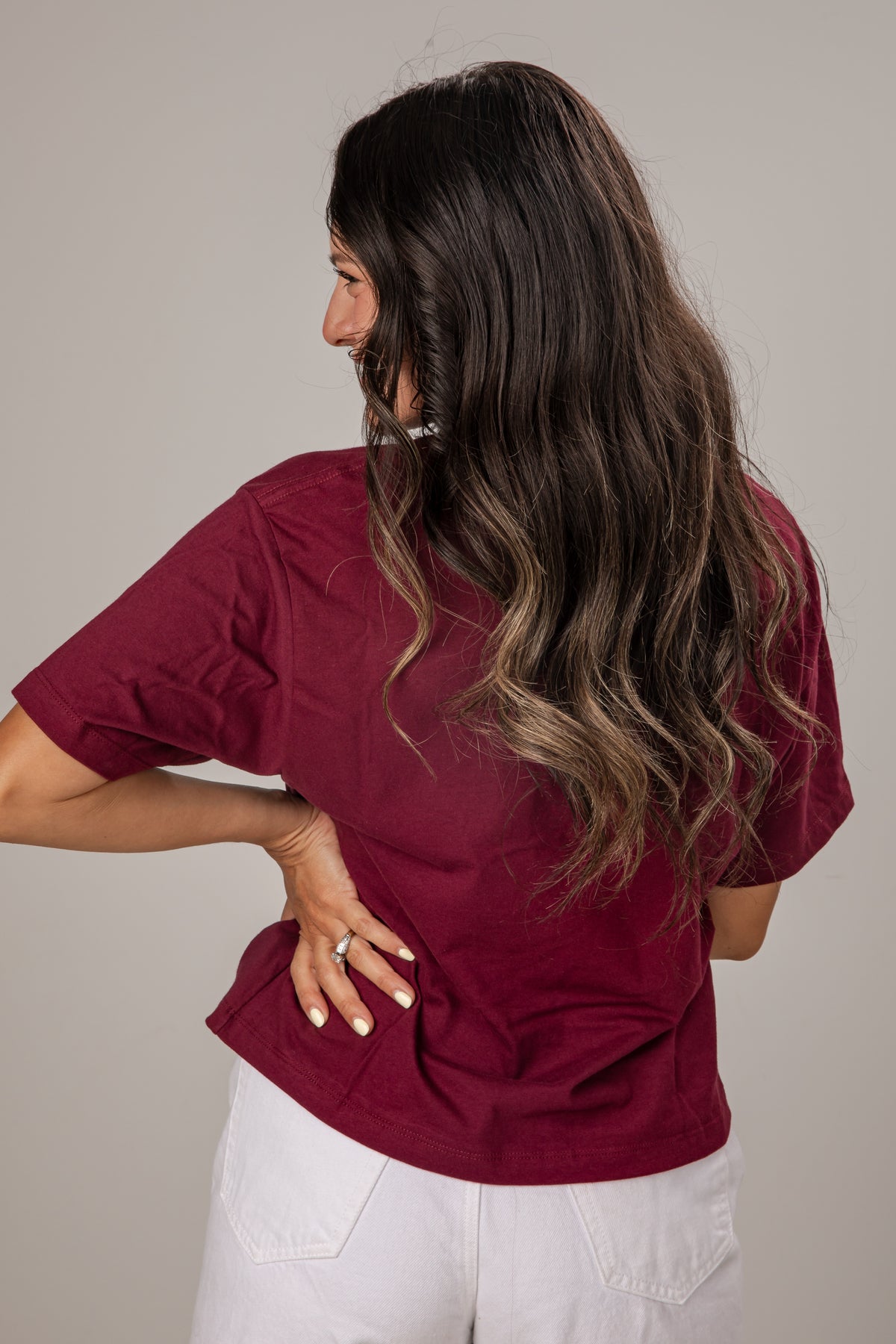 Woman wearing a burgundy shirt and white pants against a plain background