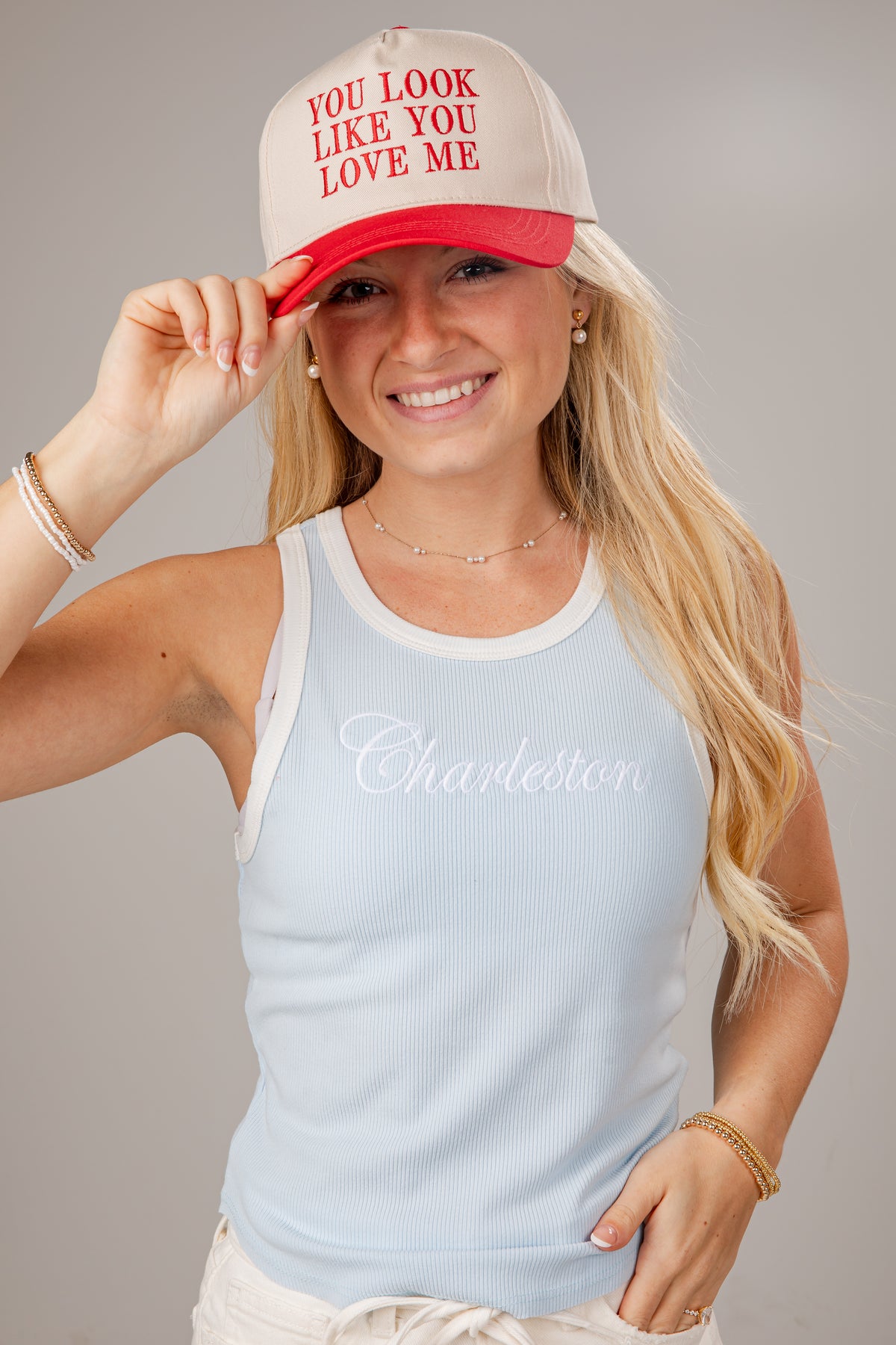 Woman wearing a red and white cap with text and a light blue tank top with &