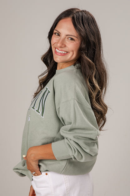 Woman wearing a green sweatshirt with text, standing against a plain background