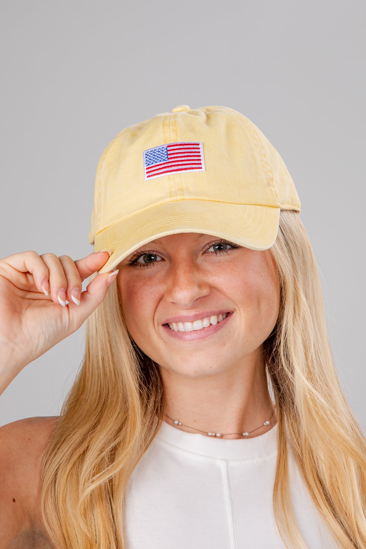 Woman wearing a yellow cap with an American flag patch on a gray background