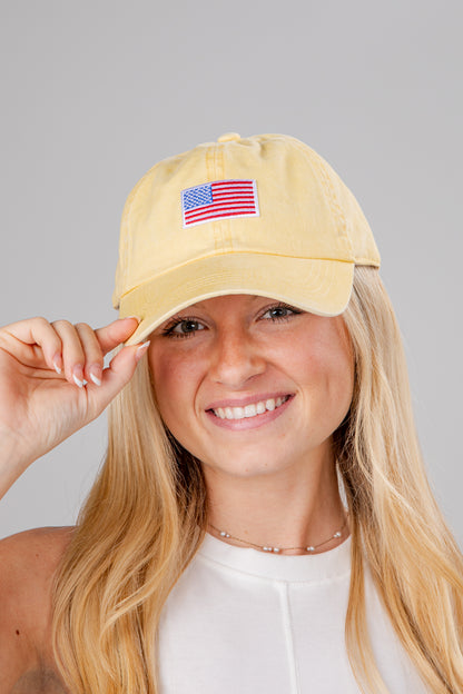 Woman wearing a yellow cap with an American flag patch on a gray background