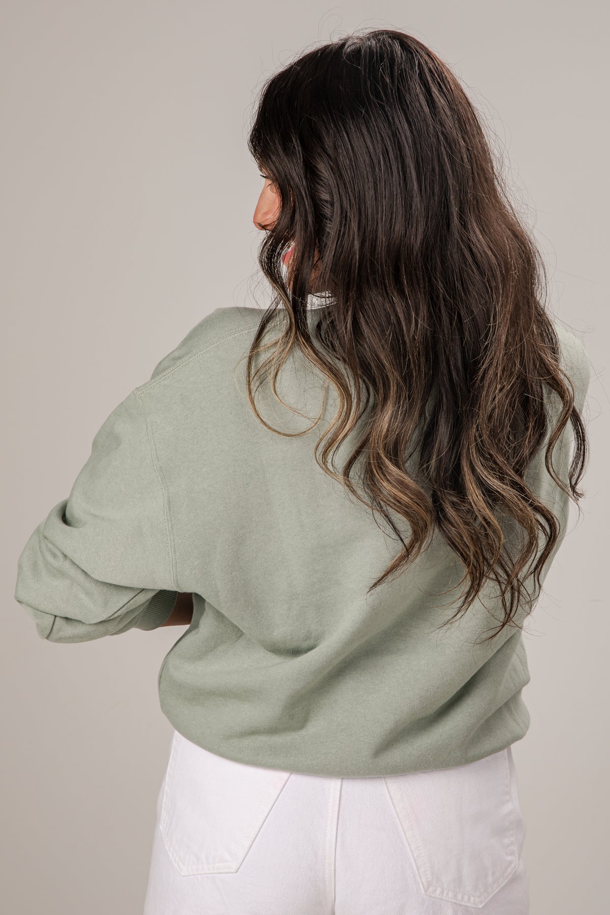Woman wearing a light green sweater and white pants against a plain background