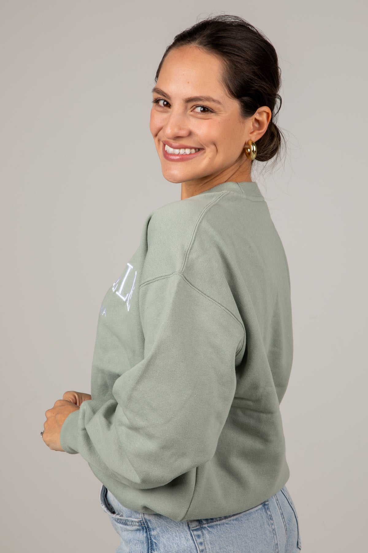 Woman wearing a light green sweatshirt with a brand logo on a plain background