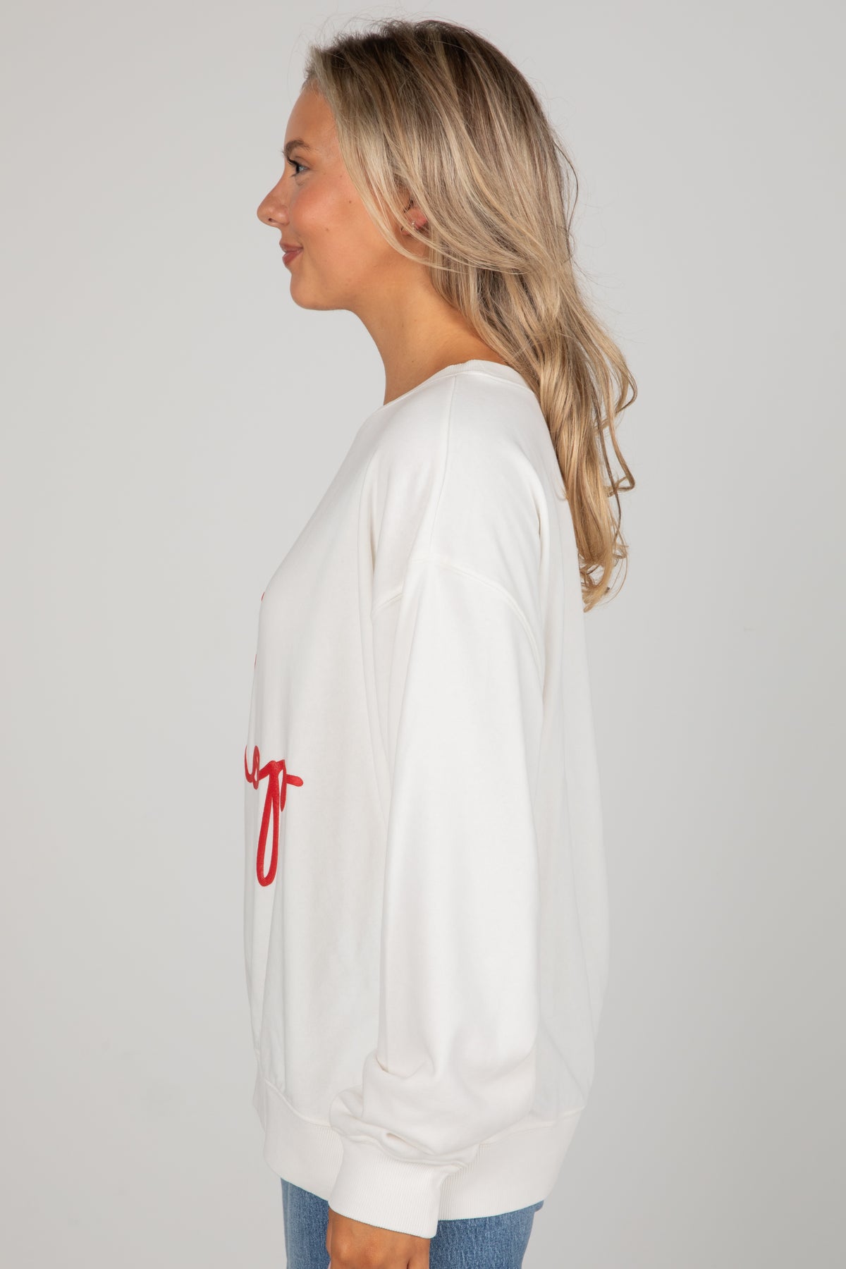 Woman wearing a white sweatshirt with red text on a plain background