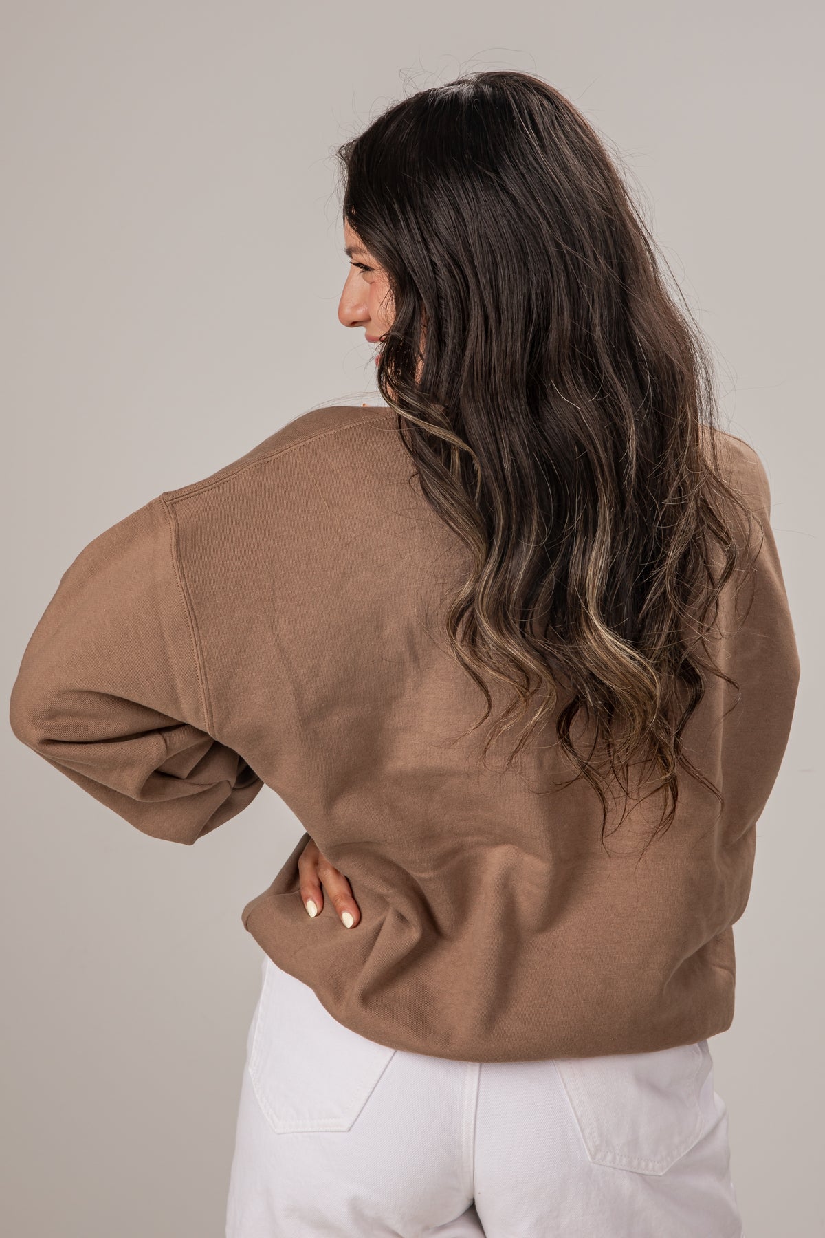 Woman wearing a brown jacket and white pants against a plain background