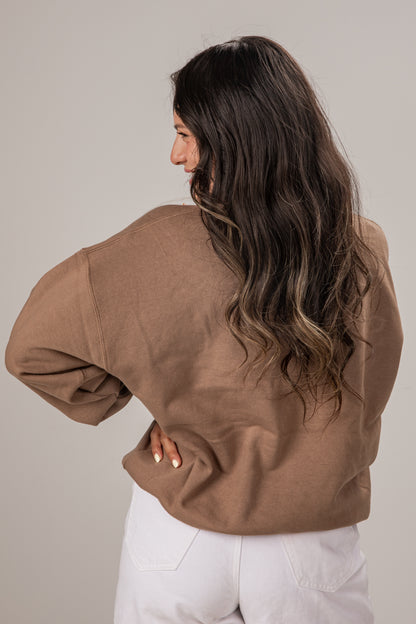 Woman wearing a brown jacket and white pants against a plain background