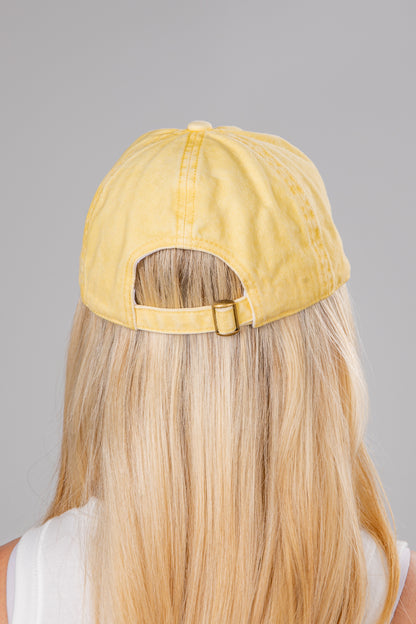 Yellow cap worn by a person with blonde hair on a gray background
