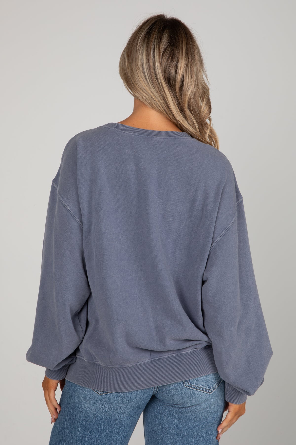 Person wearing a blue sweatshirt and jeans on a plain background