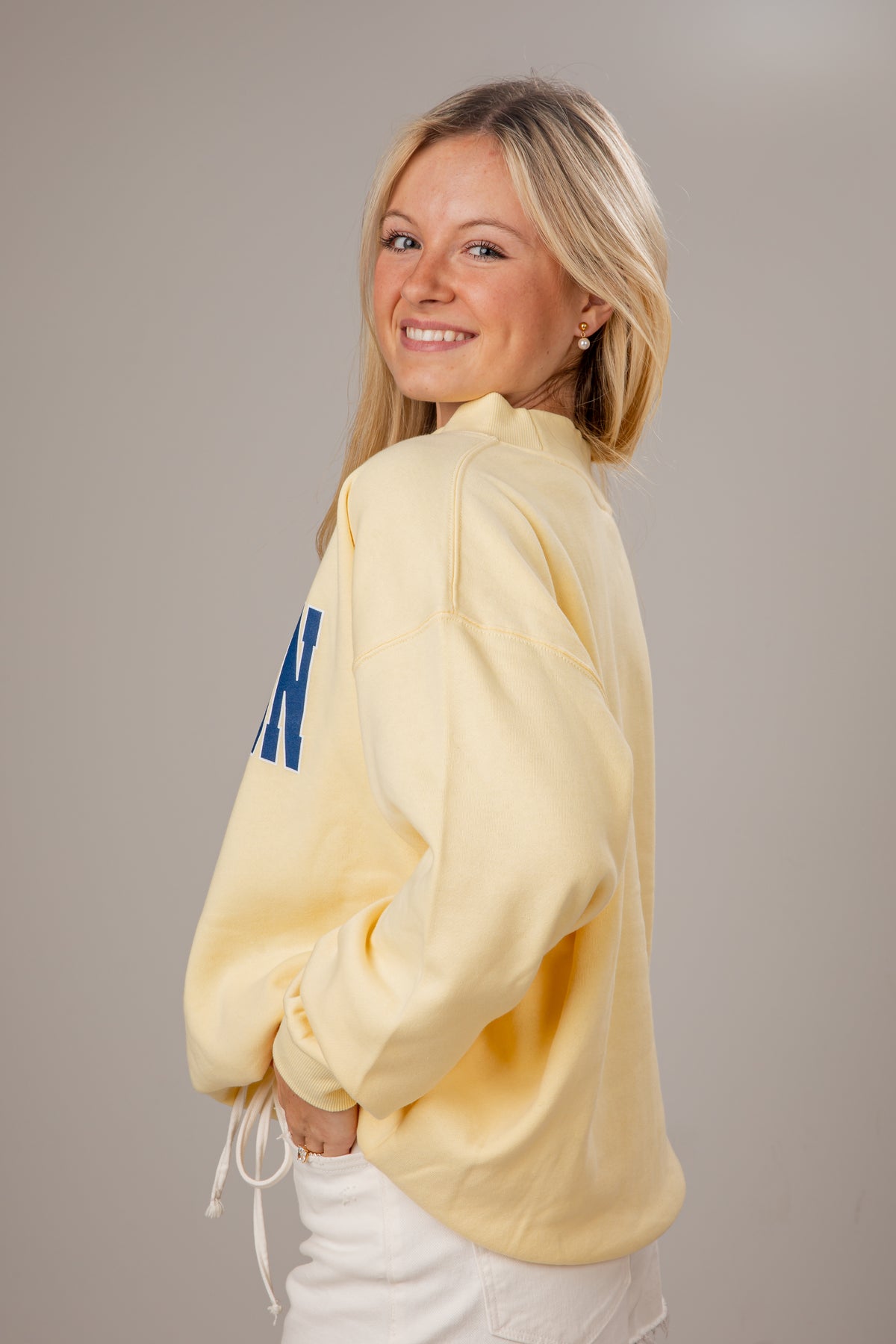 Woman wearing a yellow sweatshirt with blue lettering on a plain background