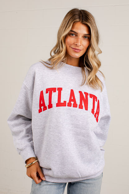A woman wearing a light heather gray crewneck sweatshirt with &