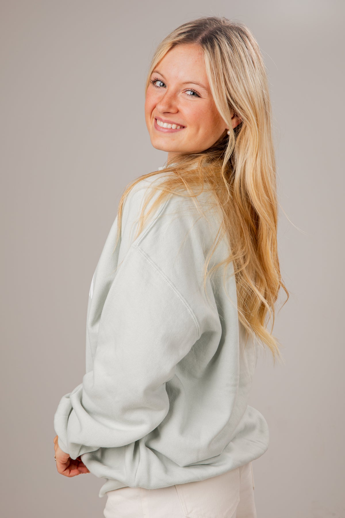 Woman wearing a light sage sweatshirt against a plain background