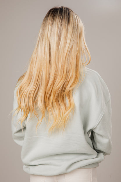 Person with long, wavy blonde hair wearing a light gray sweater against a neutral background
