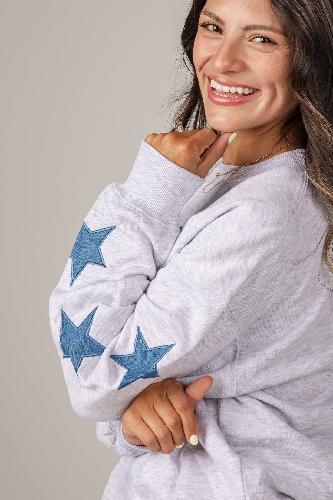 Woman wearing a gray sweater with blue star patterns on a plain background