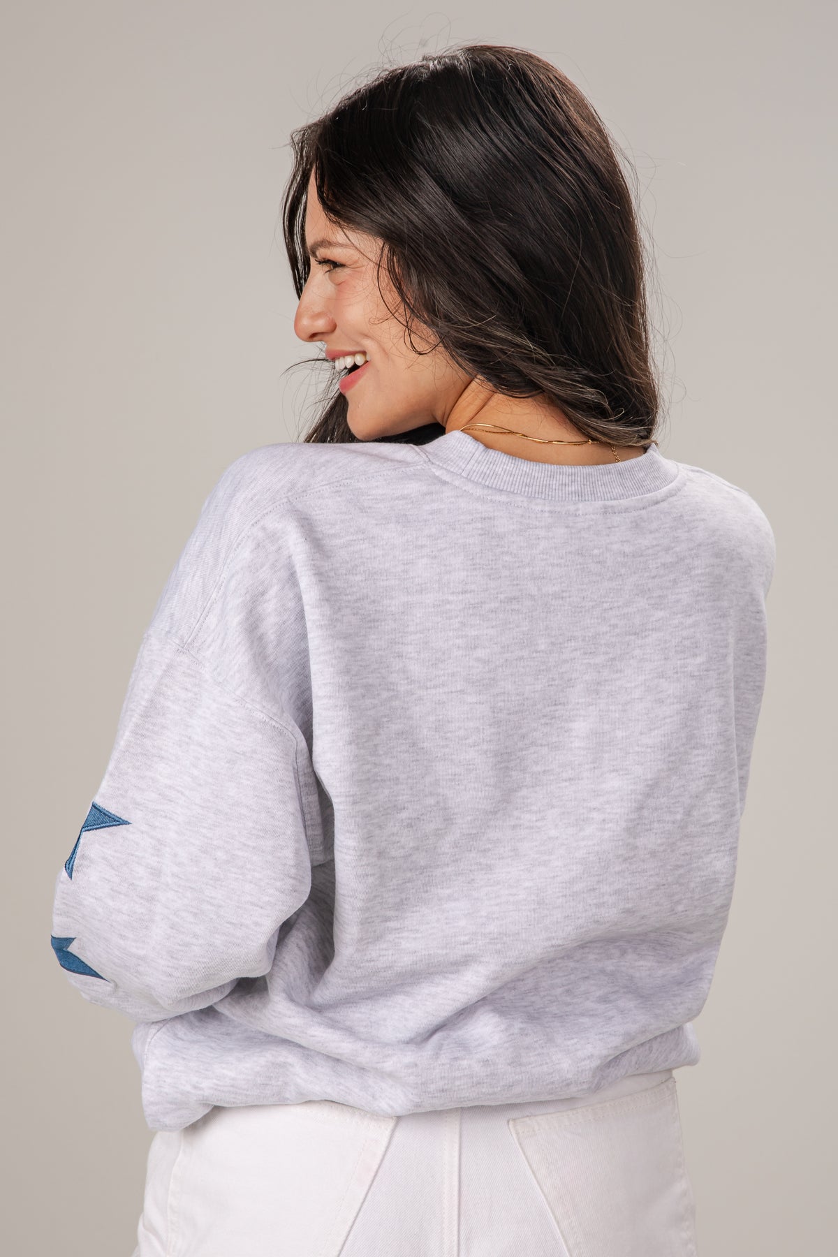 Woman wearing a light gray sweatshirt with rolled-up sleeves on a plain background