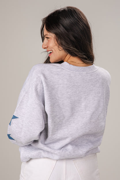 Woman wearing a light gray sweatshirt with rolled-up sleeves on a plain background