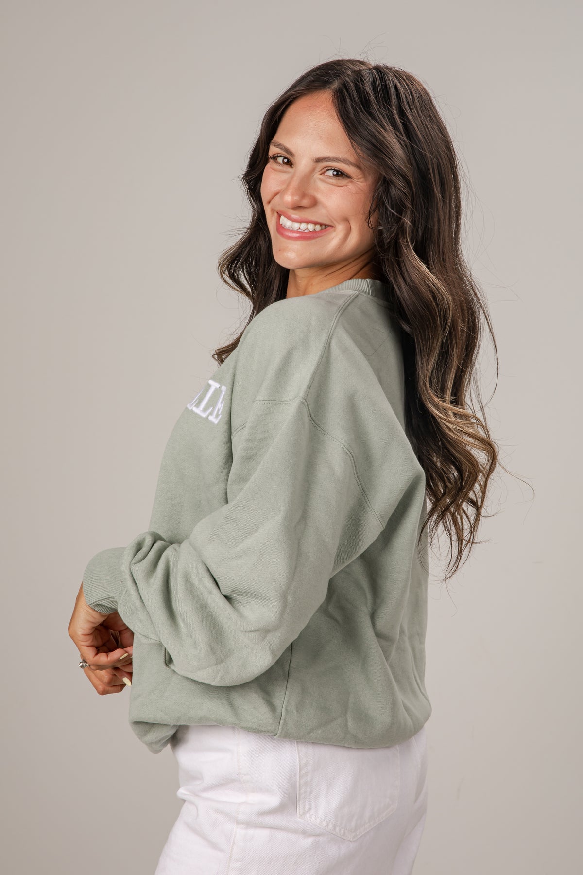 Woman wearing a green sweatshirt with text on the back, standing against a plain background
