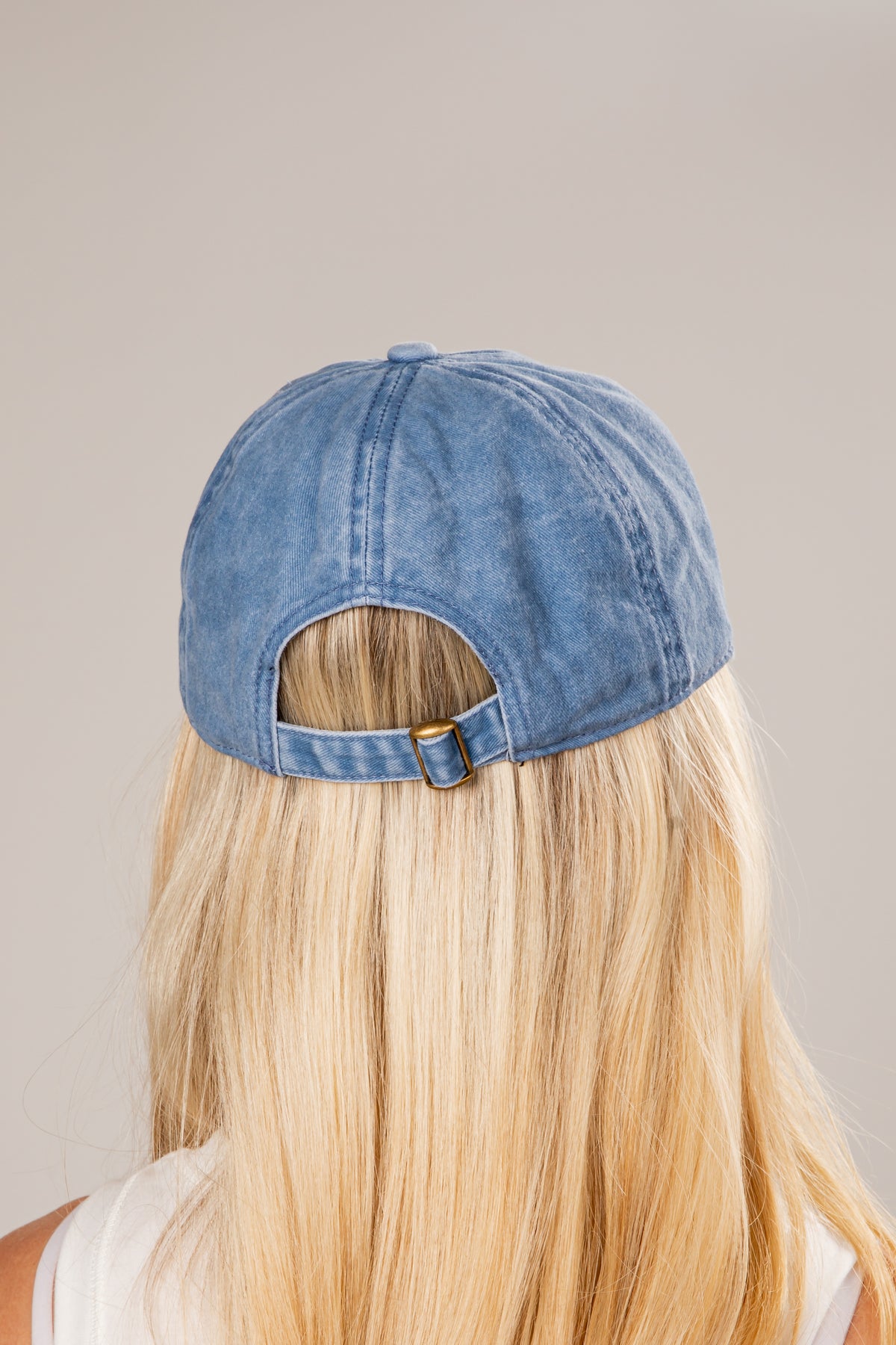 Blue denim cap worn by a person with blonde hair on a neutral background