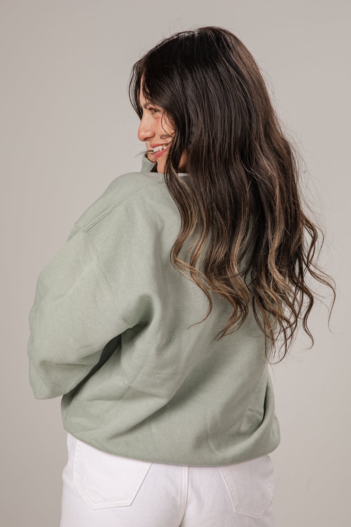 Woman wearing a light green PULLOVER and white pants against a plain background