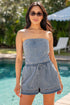 Woman wearing a denim romper standing by a pool with greenery in the background