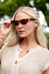 Woman wearing sunglasses outdoors with greenery in the background