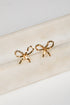 Gold bow-shaped earrings on a marble surface