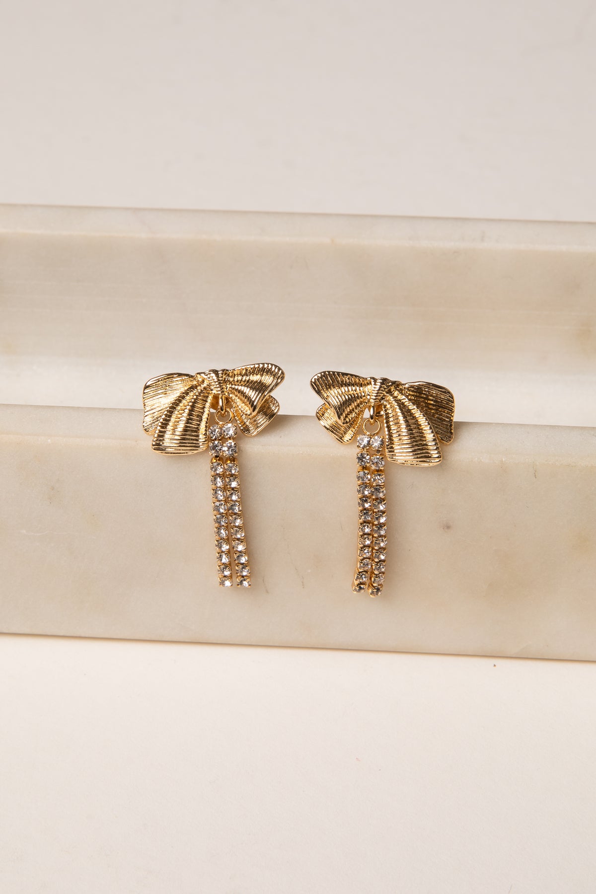 Gold bow-shaped earrings on a marble surface