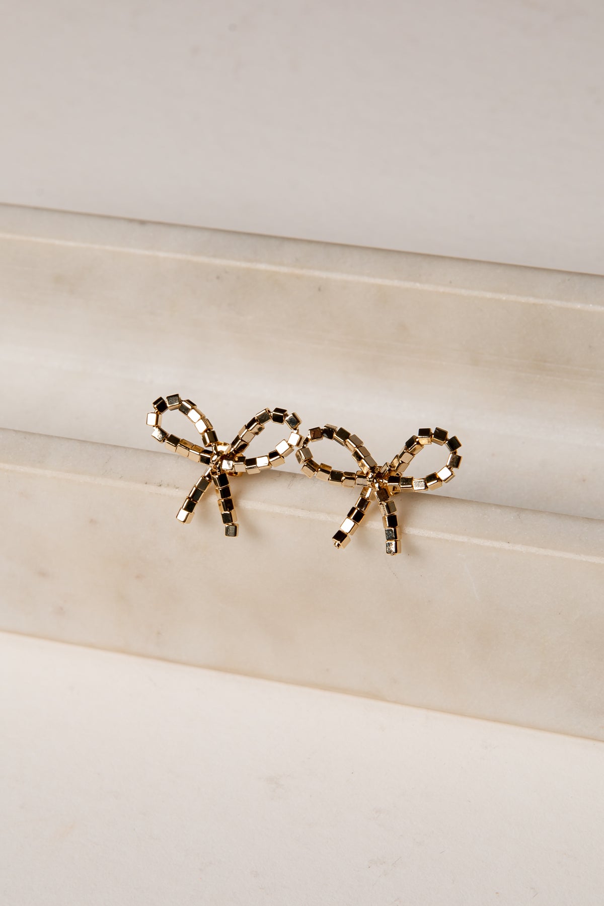 Gold bow-shaped earrings on a marble surface