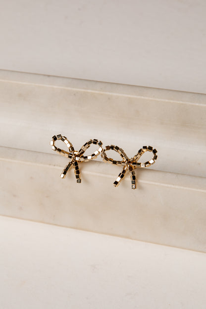 Gold bow-shaped earrings on a marble surface