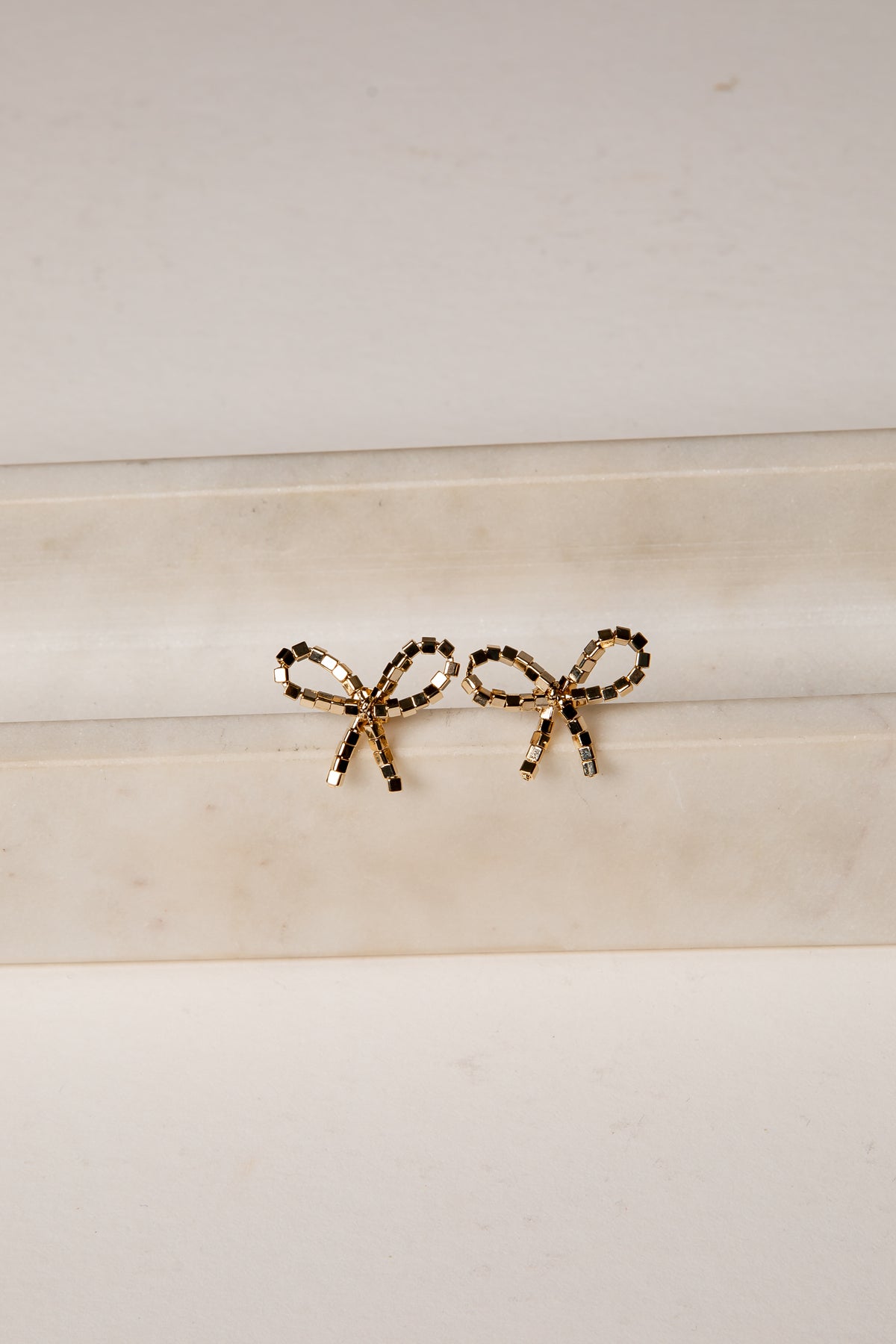 Gold bow-shaped earrings on a marble surface