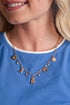 Close-up of a woman wearing a gold necklace with charms against a blue shirt.