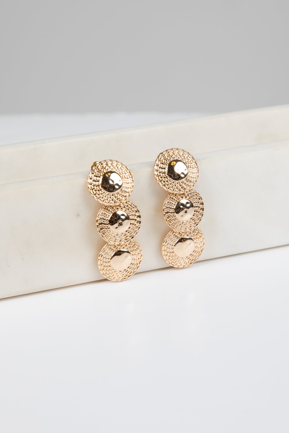 Rose gold earrings on a white surface with a gray background