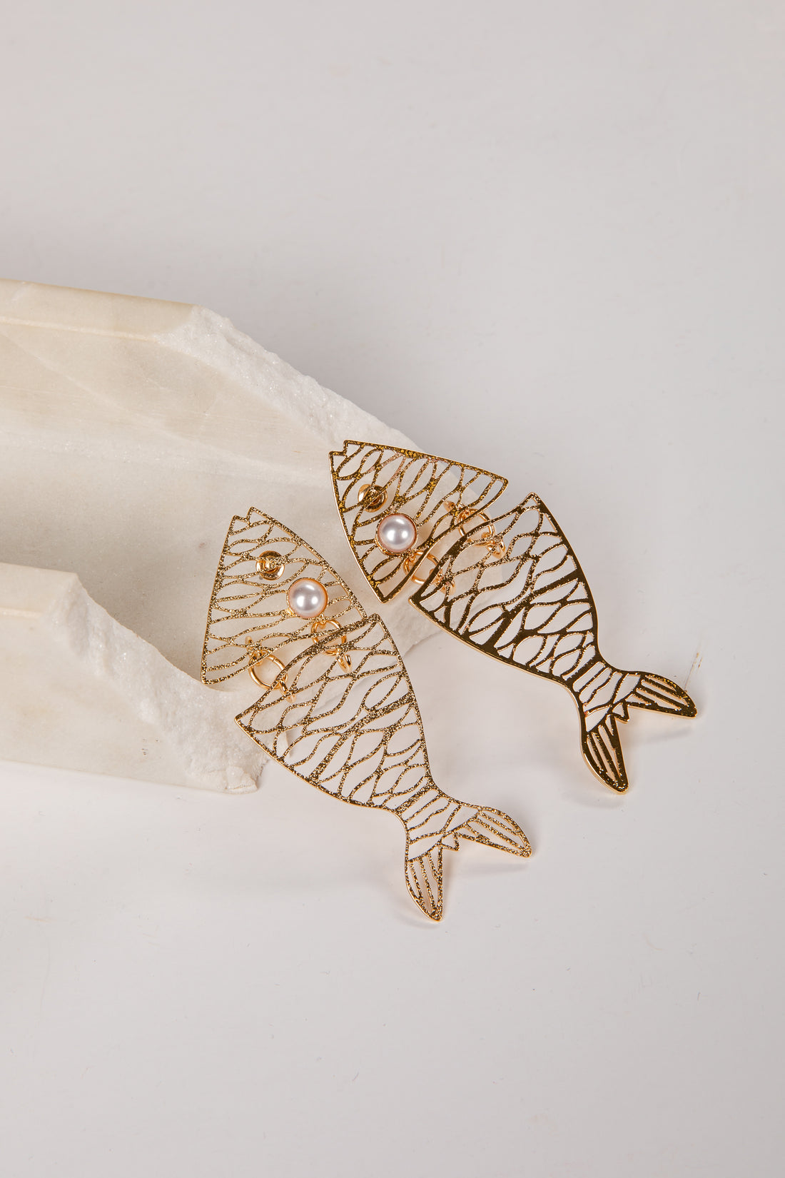 Gold fish-shaped earrings with pearl centers on a light background
