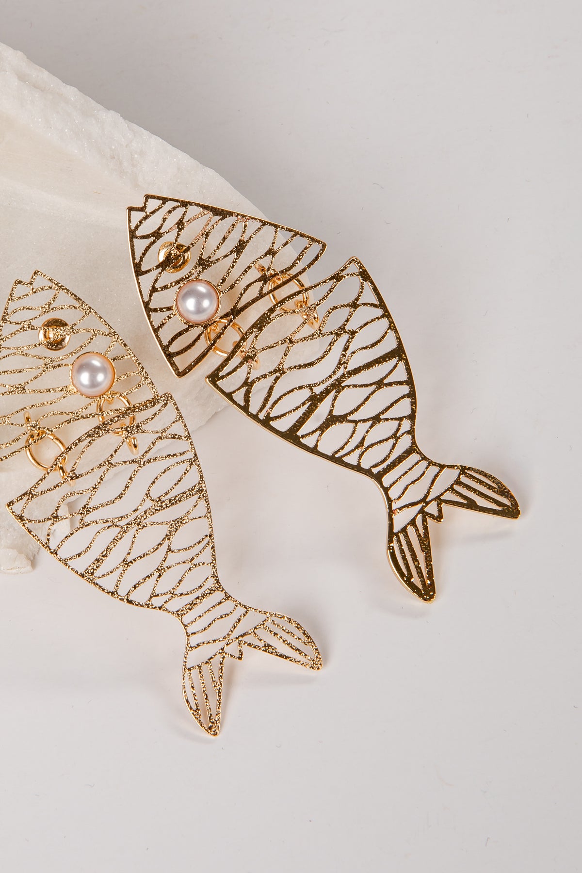 Gold fish-shaped earrings with pearl accents on a light background