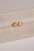 Heart-shaped gold earrings on a beige surface