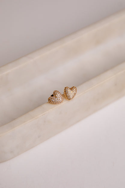 Heart-shaped gold earrings on a light beige surface